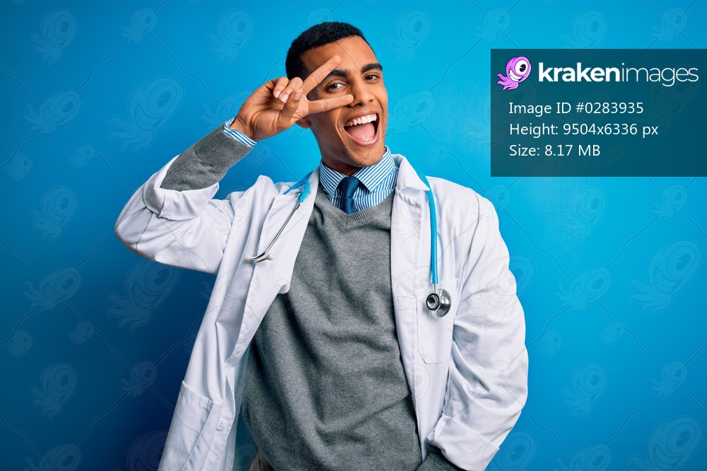 Handsome african american doctor man wearing coat and stethoscope over blue background Doing peace symbol with fingers over face, smiling cheerful showing victory
