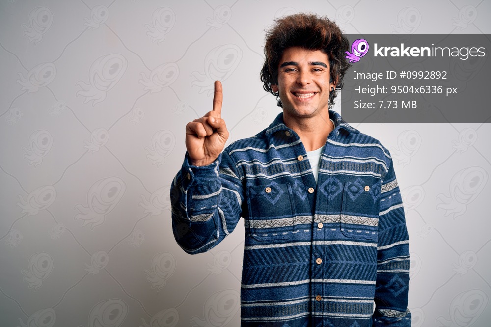 Young handsome man wearing casual shirt standing over isolated white background showing and pointing up with finger number one while smiling confident and happy.