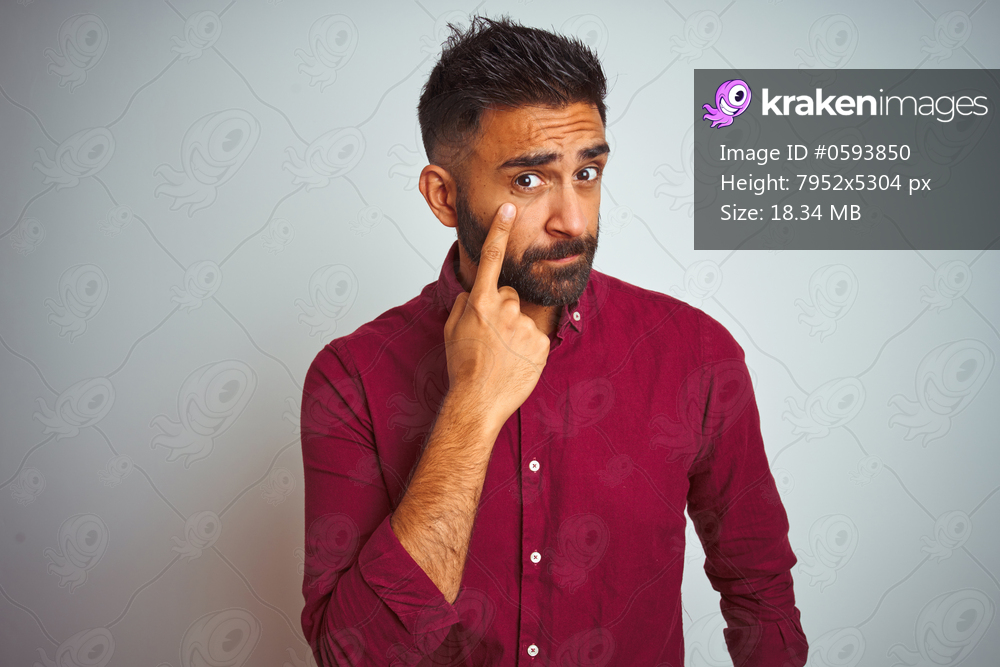 Young indian man wearing red elegant shirt standing over isolated grey background Pointing to the eye watching you gesture, suspicious expression