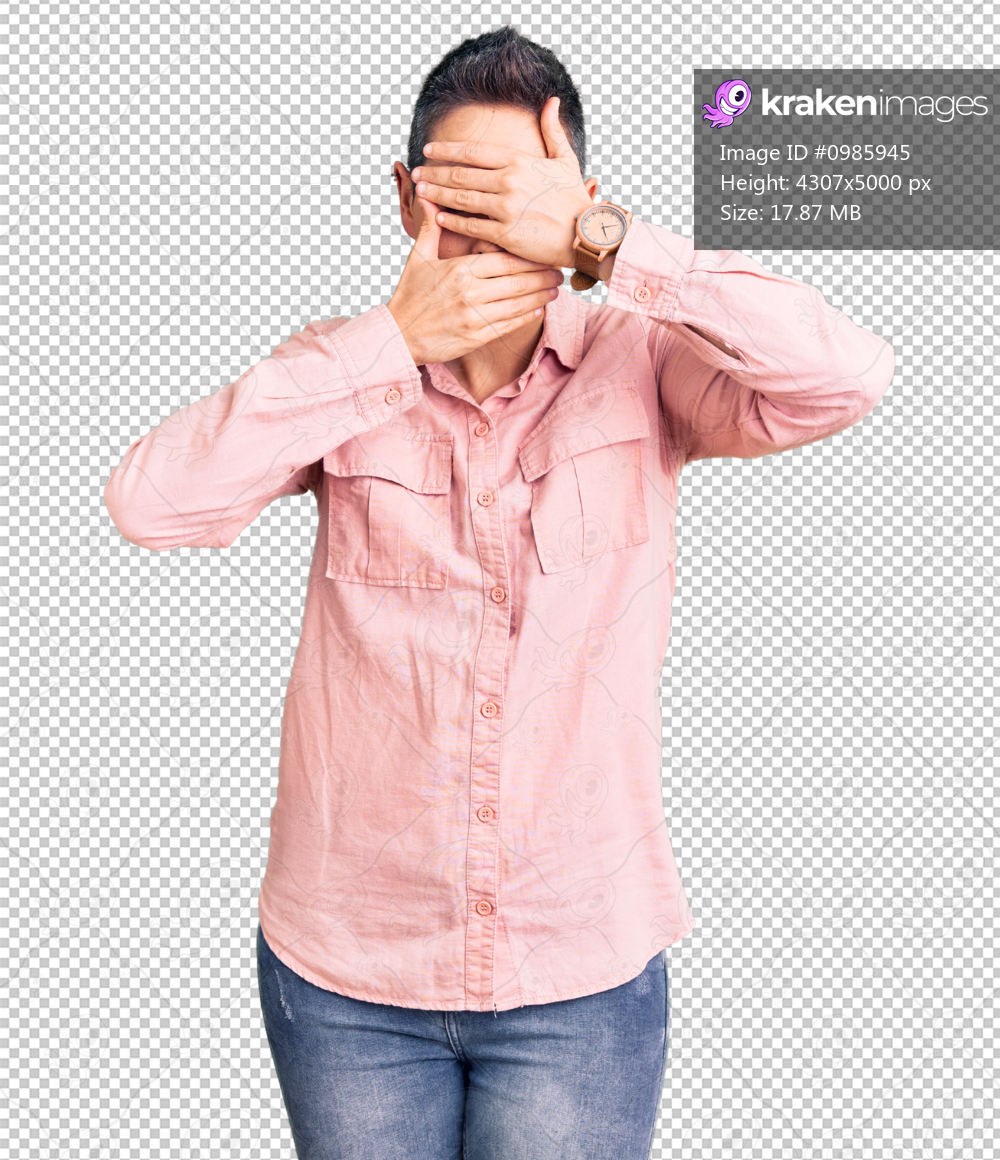 Young woman with short hair wearing casual clothes covering eyes and mouth with hands, surprised and shocked. hiding emotion