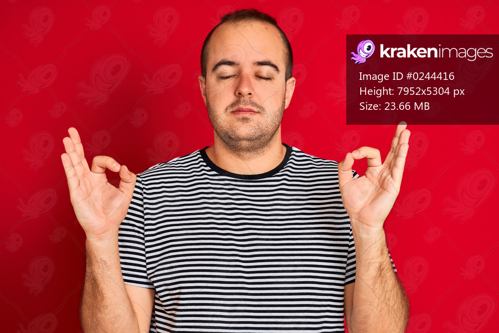 Young man wearing striped navy t-shirt standing over isolated red background relax and smiling with eyes closed doing meditation gesture with fingers. Yoga concept.