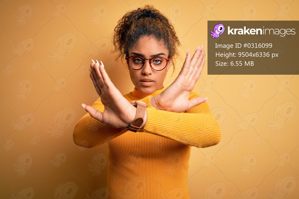 Young beautiful african american girl wearing sweater and glasses over yellow background Rejection expression crossing arms doing negative sign, angry face