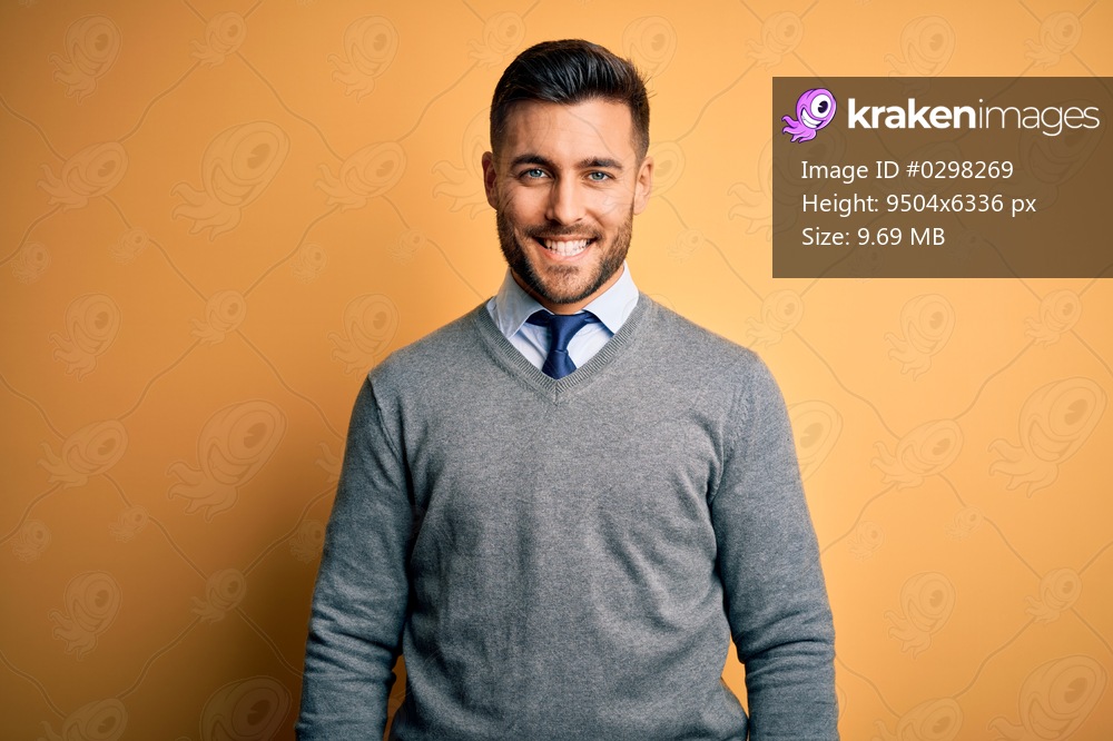 Young handsome businessman wearing elegant sweater and tie over yellow background with a happy and cool smile on face. Lucky person.