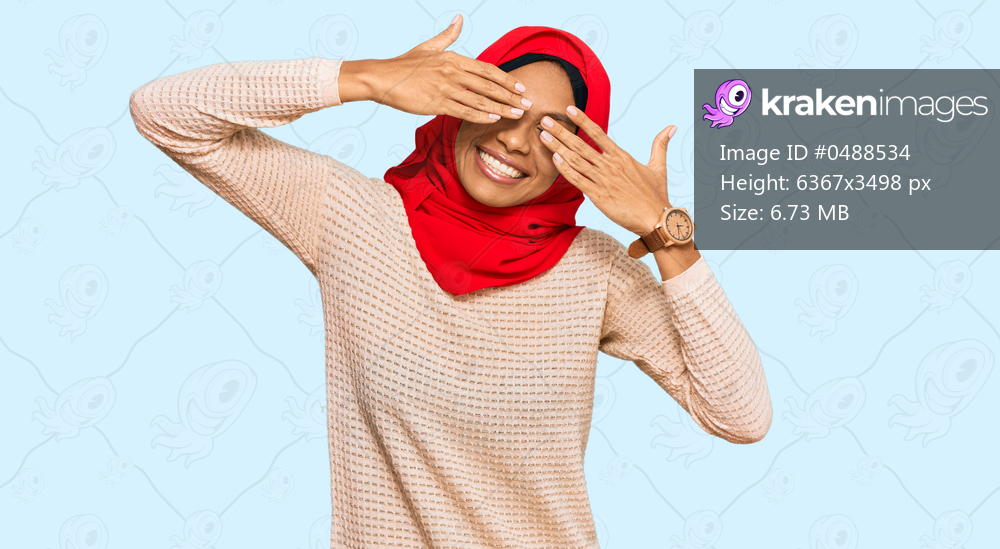 Young african american woman wearing traditional islamic hijab scarf covering eyes with hands smiling cheerful and funny. blind concept. 
