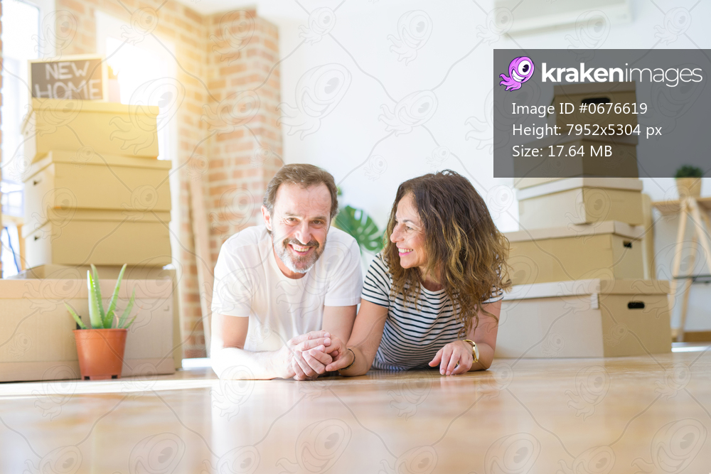 Middle age senior romantic couple lying on the floor, smiling happy for moving to a new house, relaxing and taking a break of packing boxes