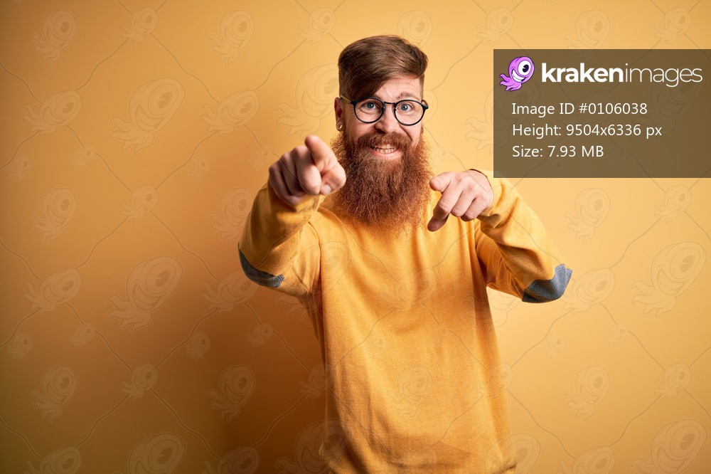 Handsome Irish redhead man with beard wearing glasses over yellow isolated background pointing to you and the camera with fingers, smiling positive and cheerful