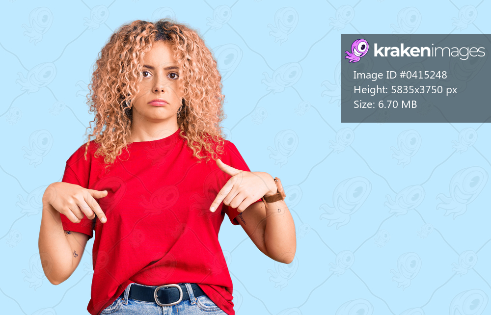 Young blonde woman with curly hair wearing casual red tshirt pointing down looking sad and upset, indicating direction with fingers, unhappy and depressed. 