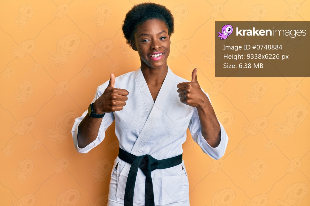 Young african american girl wearing karate kimono and black belt success sign doing positive gesture with hand, thumbs up smiling and happy. cheerful expression and winner gesture. 