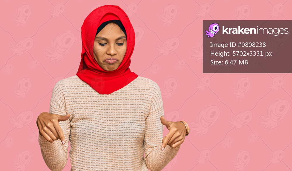 Young african american woman wearing traditional islamic hijab scarf pointing down looking sad and upset, indicating direction with fingers, unhappy and depressed. 