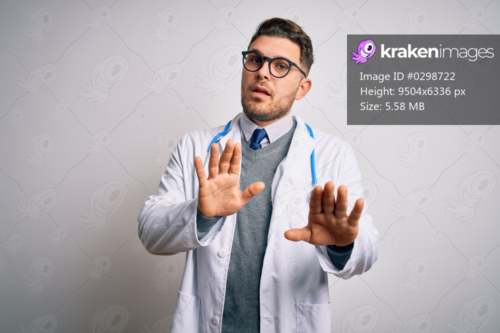 Young doctor man with blue eyes wearing medical coat and stethoscope over isolated background Moving away hands palms showing refusal and denial with afraid and disgusting expression. Stop and forbidden.
