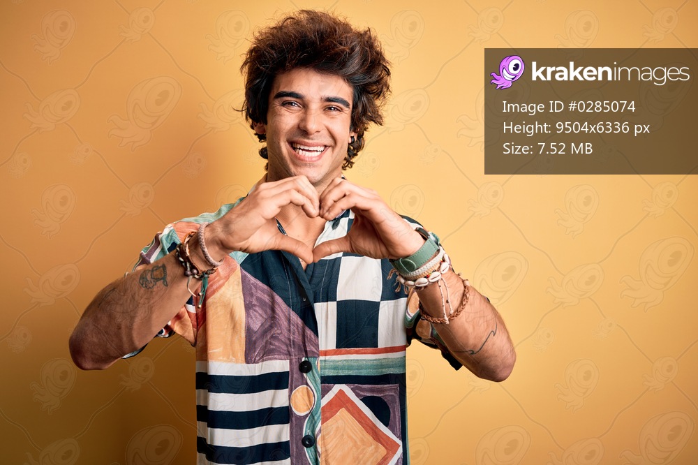 Young handsome man on vacation wearing summer shirt over isolated yellow background smiling in love doing heart symbol shape with hands. Romantic concept.