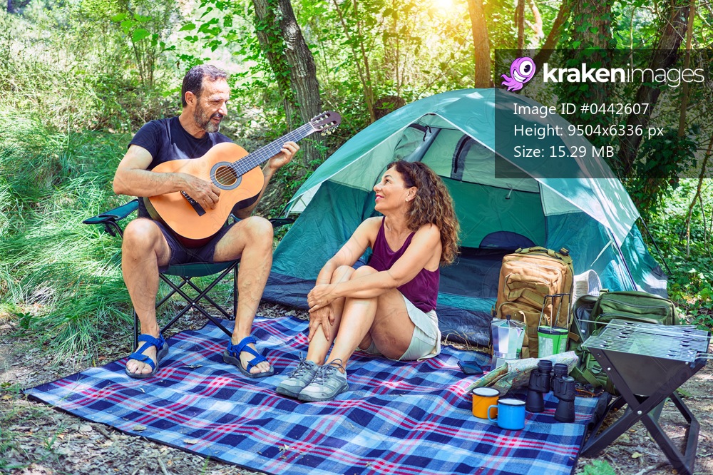 Middle age couple  of hiker smiling happy camping at the forest. Sitting on the floor singing song playing classical guitar