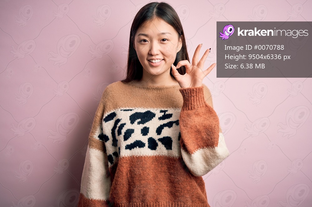 Young beautiful asian woman wearing animal print fashion sweater over pink isolated background smiling positive doing ok sign with hand and fingers. Successful expression.