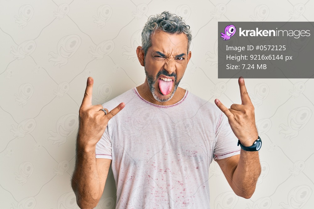 Middle age grey-haired man wearing casual clothes shouting with crazy expression doing rock symbol with hands up. music star. heavy concept. 