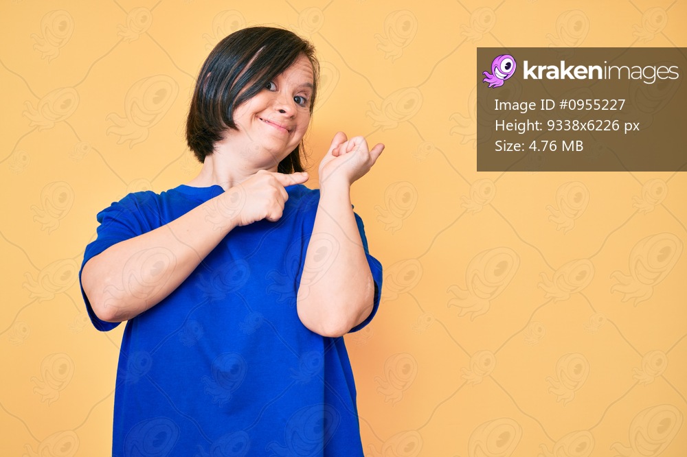 Brunette woman with down syndrome wearing casual clothes smiling and looking at the camera pointing with two hands and fingers to the side. 