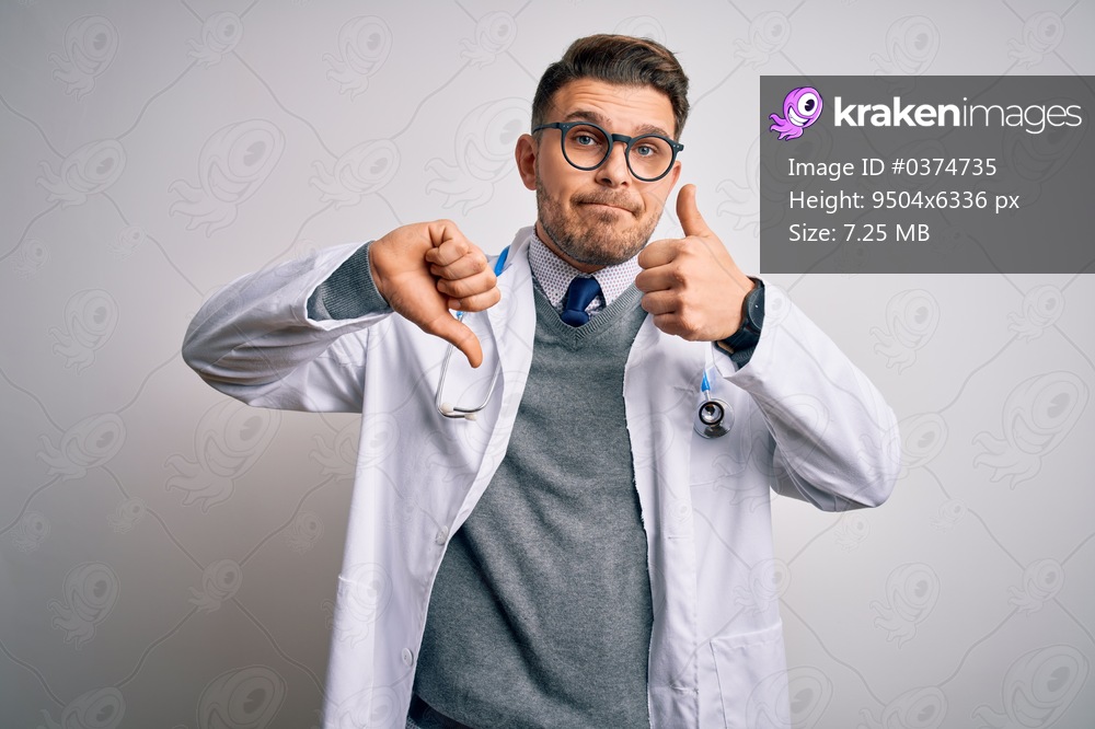 Young doctor man with blue eyes wearing medical coat and stethoscope over isolated background Doing thumbs up and down, disagreement and agreement expression. Crazy conflict