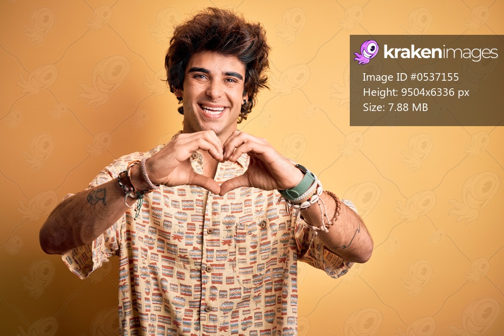 Young handsome man on vacation wearing summer shirt over isolated yellow background smiling in love doing heart symbol shape with hands. Romantic concept.