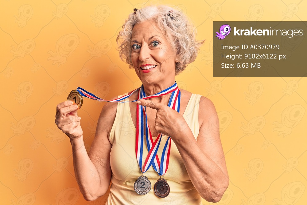Senior grey-haired woman wearing medals smiling happy pointing with hand and finger 