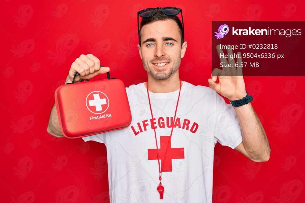 Young handsome lifeguard man wearing t-shirt with red cross and whistle holding first aid kit doing ok sign with fingers, excellent symbol