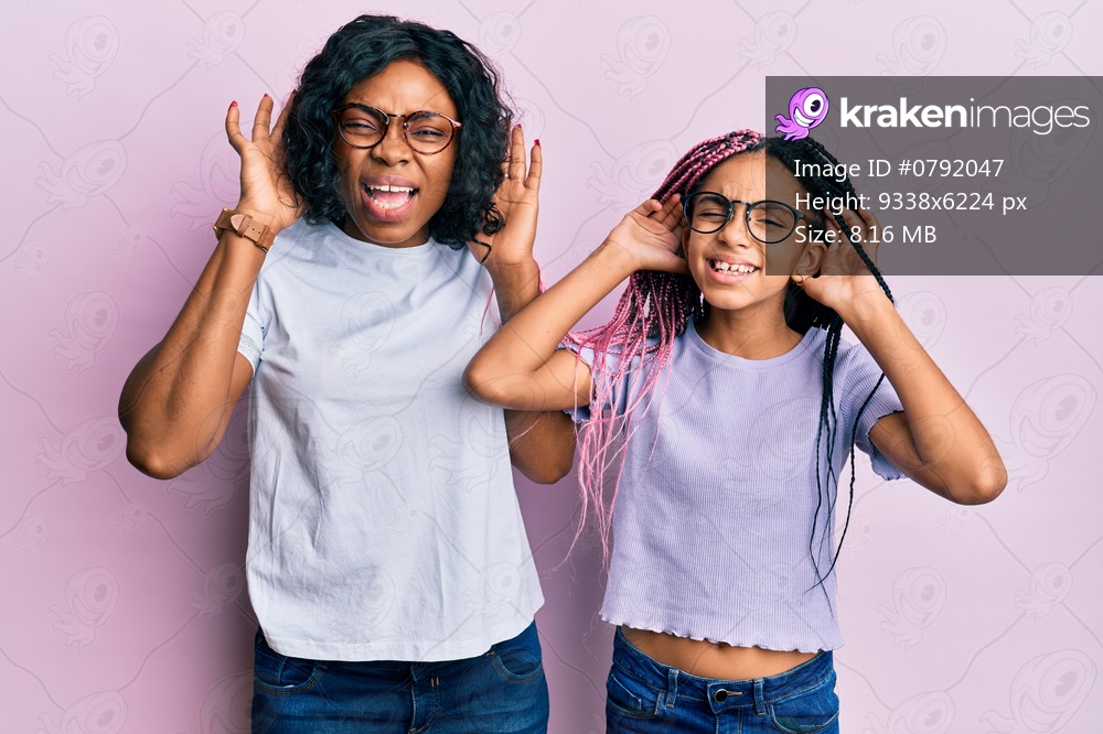 Beautiful african american mother and daughter wearing casual clothes and glasses trying to hear both hands on ear gesture, curious for gossip. hearing problem, deaf 