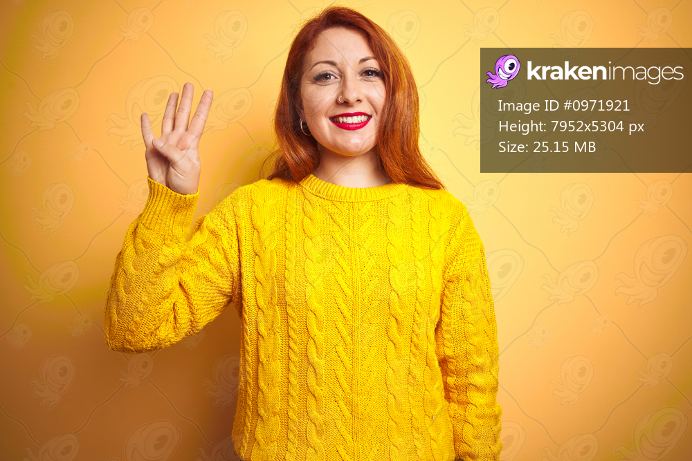 Beautiful redhead woman wearing winter sweater standing over isolated yellow background showing and pointing up with fingers number four while smiling confident and happy.