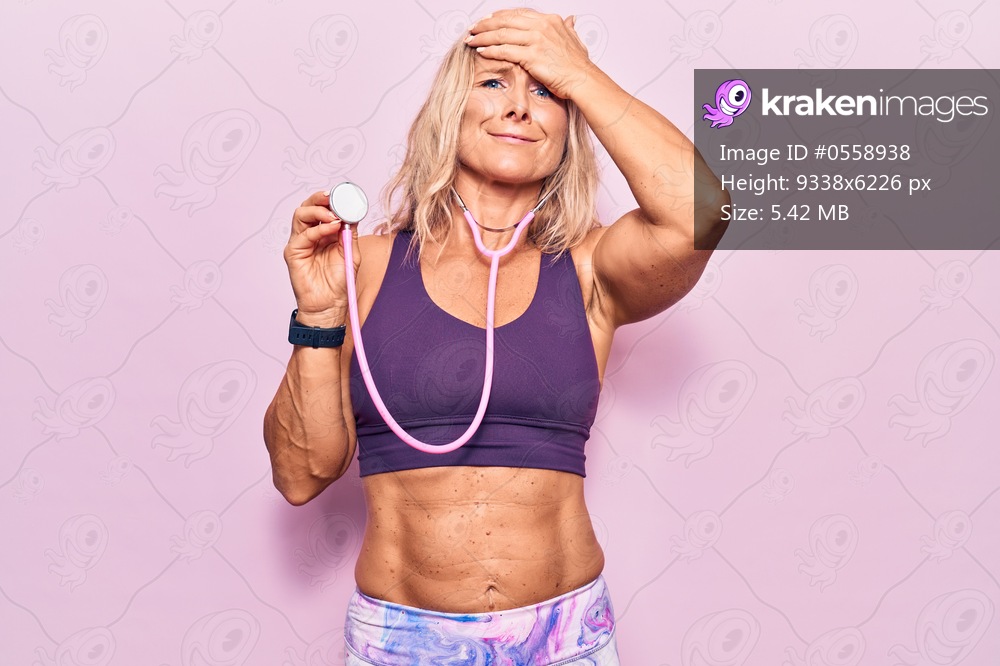Middle age caucasian blonde woman wearing sport clothes holding stethoscope stressed and frustrated with hand on head, surprised and angry face 
