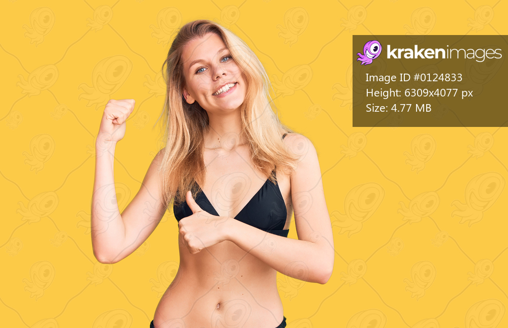 Young beautiful blonde woman wearing bikini pointing to the back behind with hand and thumbs up, smiling confident 