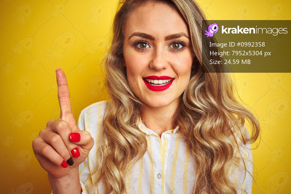 Young beautiful woman wearing stripes shirt standing over yellow isolated background surprised with an idea or question pointing finger with happy face, number one