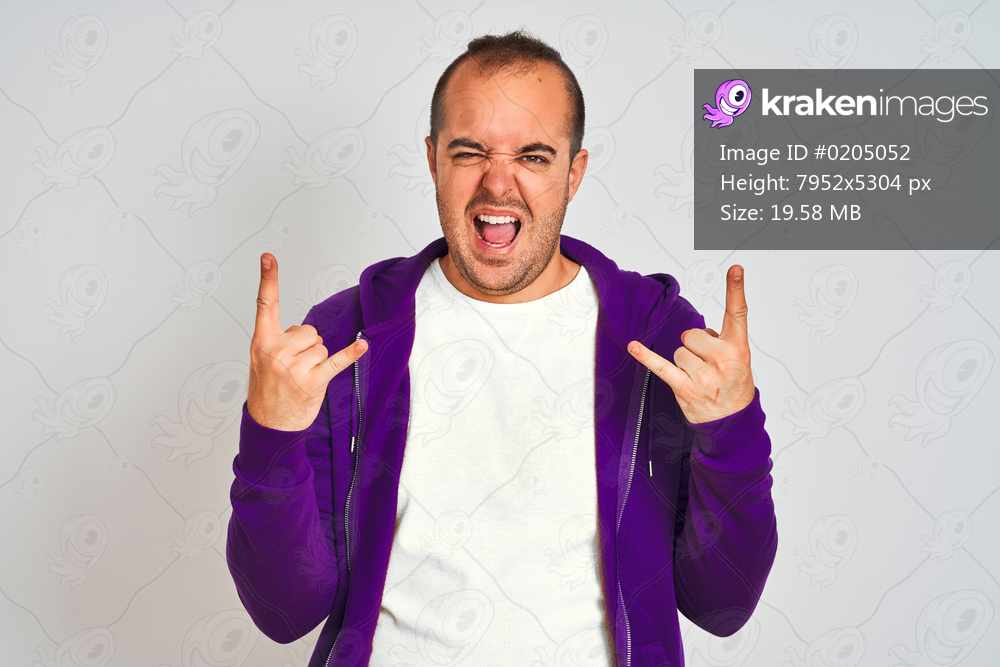 Young man wearing purple sweatshirt standing over isolated white background shouting with crazy expression doing rock symbol with hands up. Music star. Heavy concept.