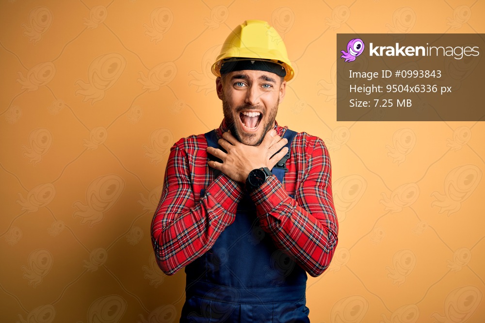 Young builder man wearing construction uniform and safety helmet over yellow isolated background shouting and suffocate because painful strangle. Health problem. Asphyxiate and suicide concept.