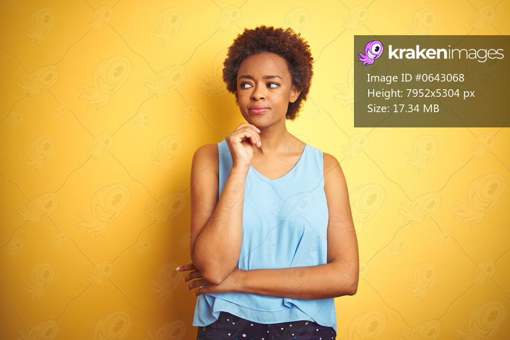 Beautiful african american woman wearing elegant shirt over isolated yellow background with hand on chin thinking about question, pensive expression. Smiling with thoughtful face. Doubt concept.