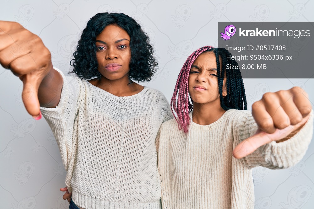 Beautiful african american mother and daughter wearing casual clothes and hugging looking unhappy and angry showing rejection and negative with thumbs down gesture. bad expression. 