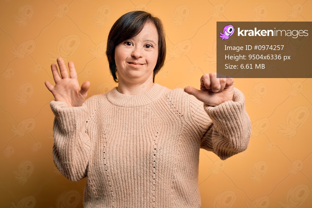 Young down syndrome woman wearing casual sweater over yellow background showing and pointing up with fingers number six while smiling confident and happy.