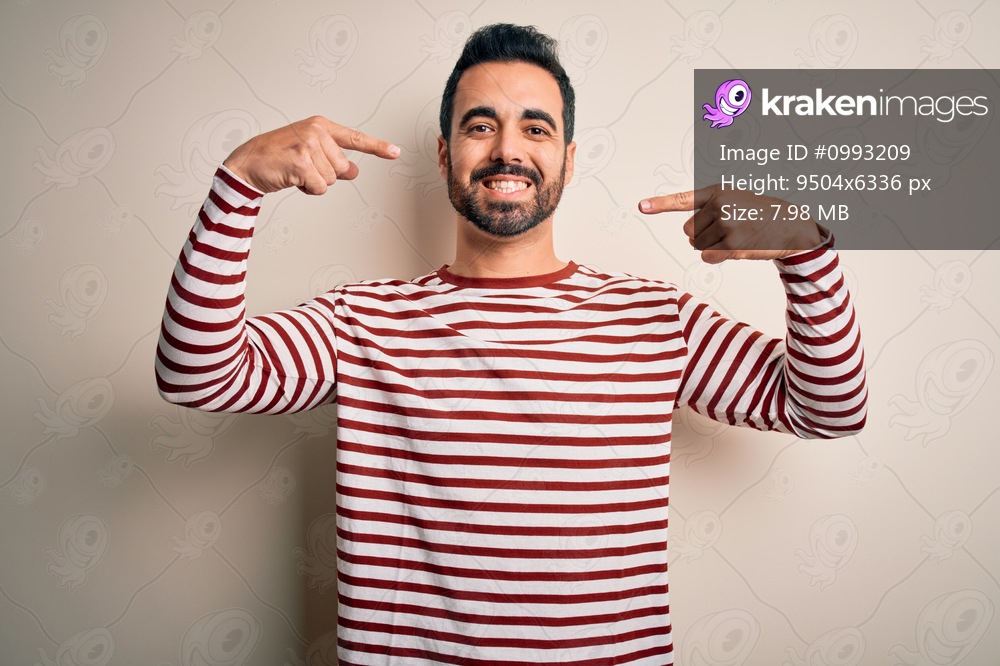 Young handsome man with beard wearing casual striped t-shirt standing over white background smiling cheerful showing and pointing with fingers teeth and mouth. Dental health concept.