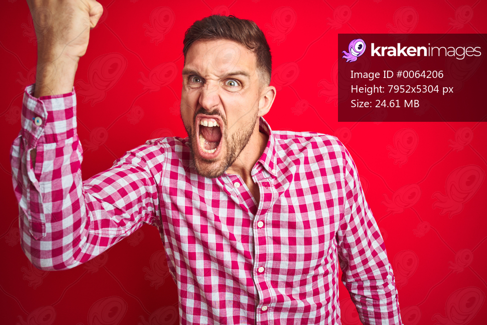 Young handsome man over red isolated background angry and mad raising fist frustrated and furious while shouting with anger. Rage and aggressive concept.