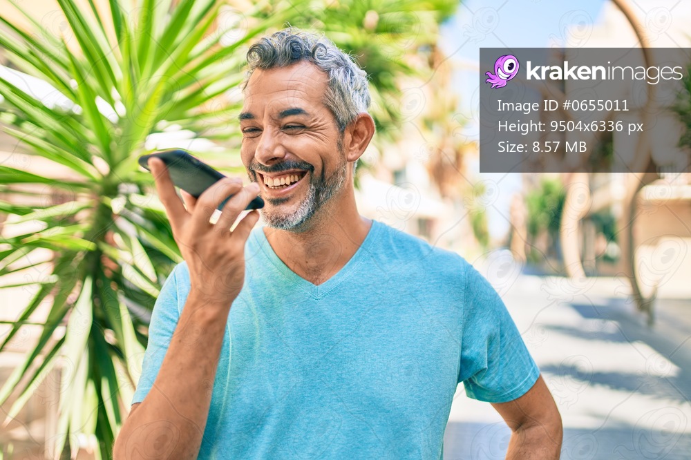 Middle age grey-haired man talking on the smartphone walking at street of city.