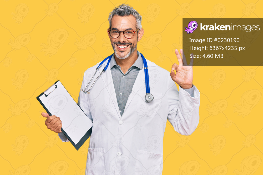 Middle age grey-haired man wearing doctor stethoscope holding clipboard doing ok sign with fingers, smiling friendly gesturing excellent symbol 
