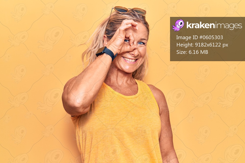Middle age caucasian blonde woman wearing casual summer clothes and sunglasses smiling happy doing ok sign with hand on eye looking through fingers 