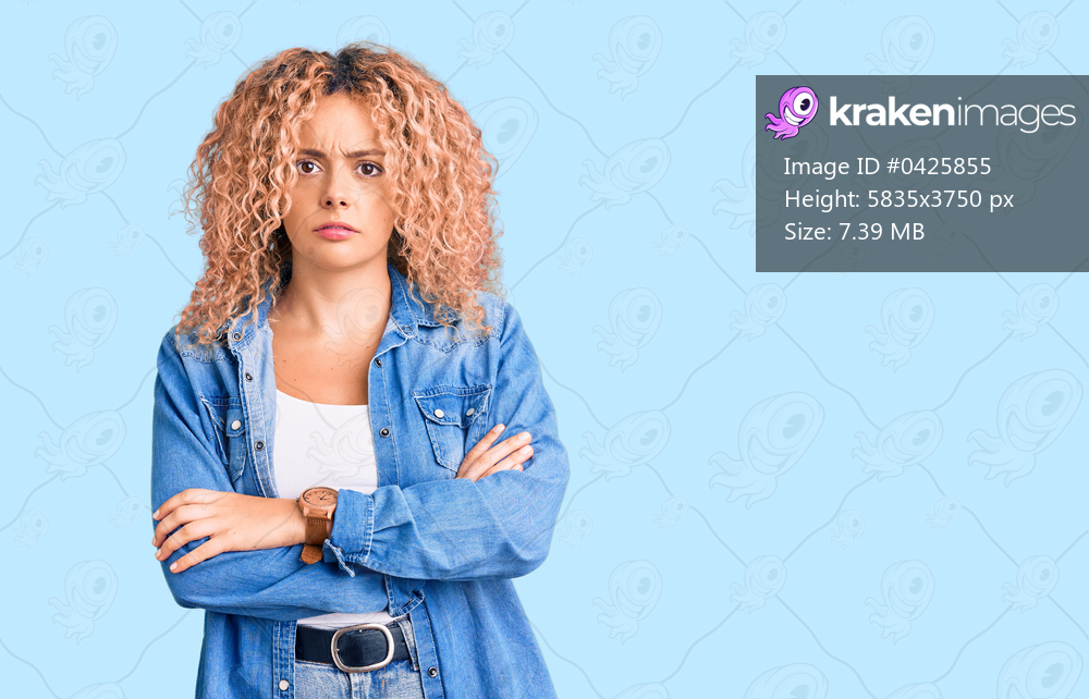 Young blonde woman with curly hair wearing casual denim jacket skeptic and nervous, disapproving expression on face with crossed arms. negative person. 