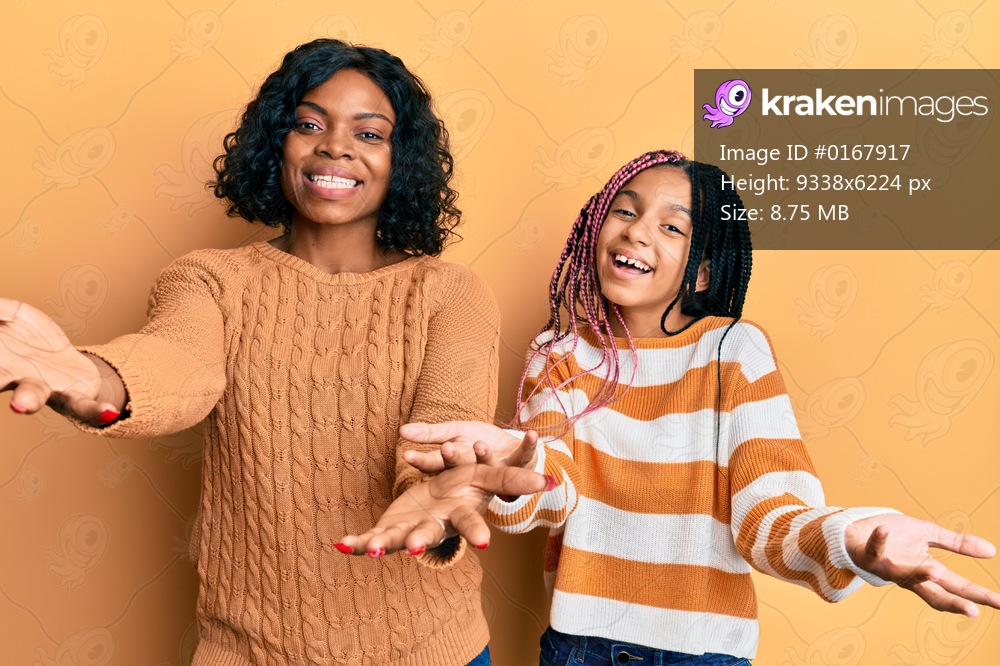 Beautiful african american mother and daughter wearing wool winter sweater smiling cheerful offering hands giving assistance and acceptance. 