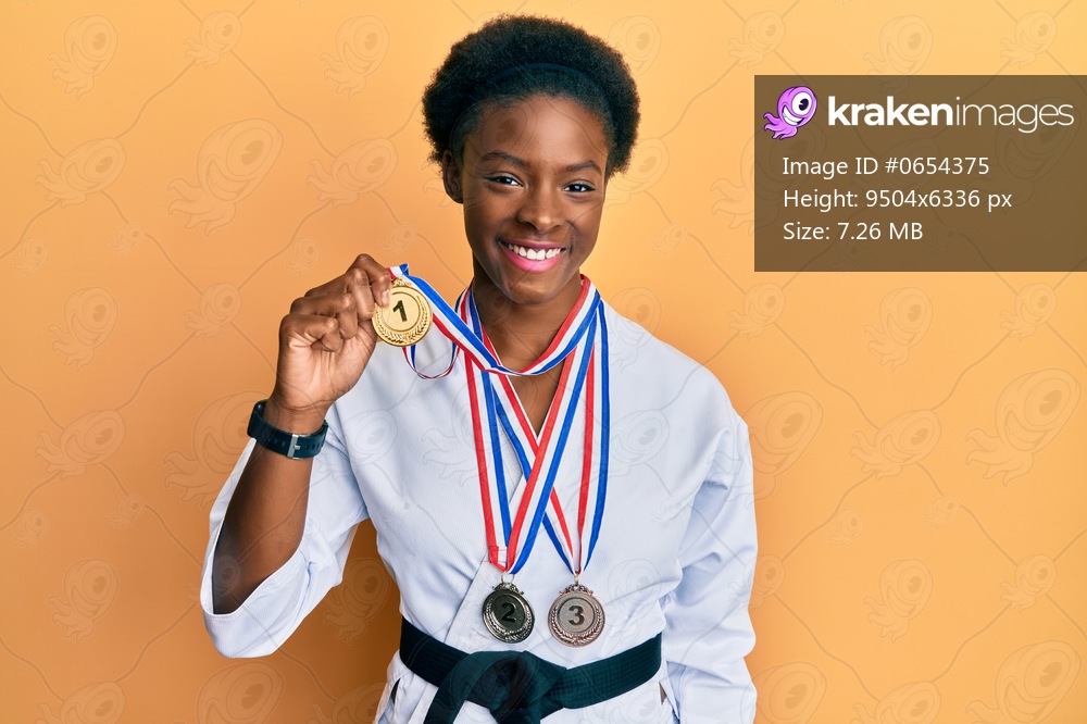 Young african american girl wearing karate kimono and black belt looking positive and happy standing and smiling with a confident smile showing teeth 