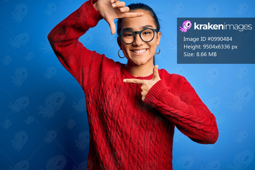Young beautiful asian woman wearing casual sweater and glasses over blue background smiling making frame with hands and fingers with happy face. Creativity and photography concept.