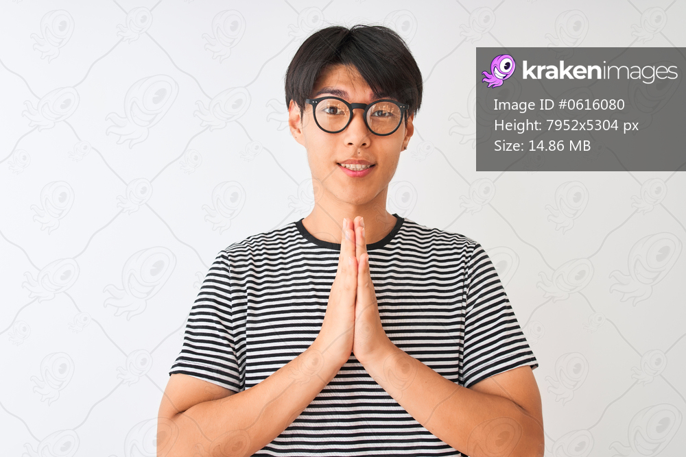 Chinese man wearing glasses and navy striped t-shirt standing over isolated white background praying with hands together asking for forgiveness smiling confident.