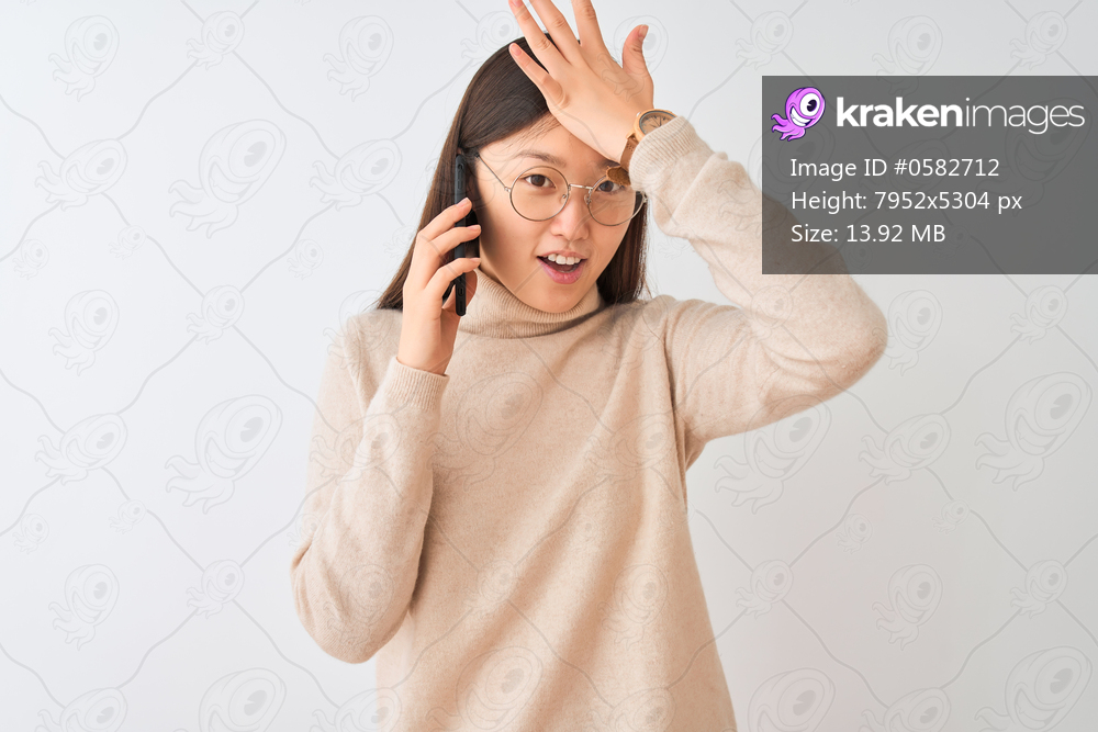 Young chinese woman talking on the smartphone over isolated white background surprised with hand on head for mistake, remember error. Forgot, bad memory concept.