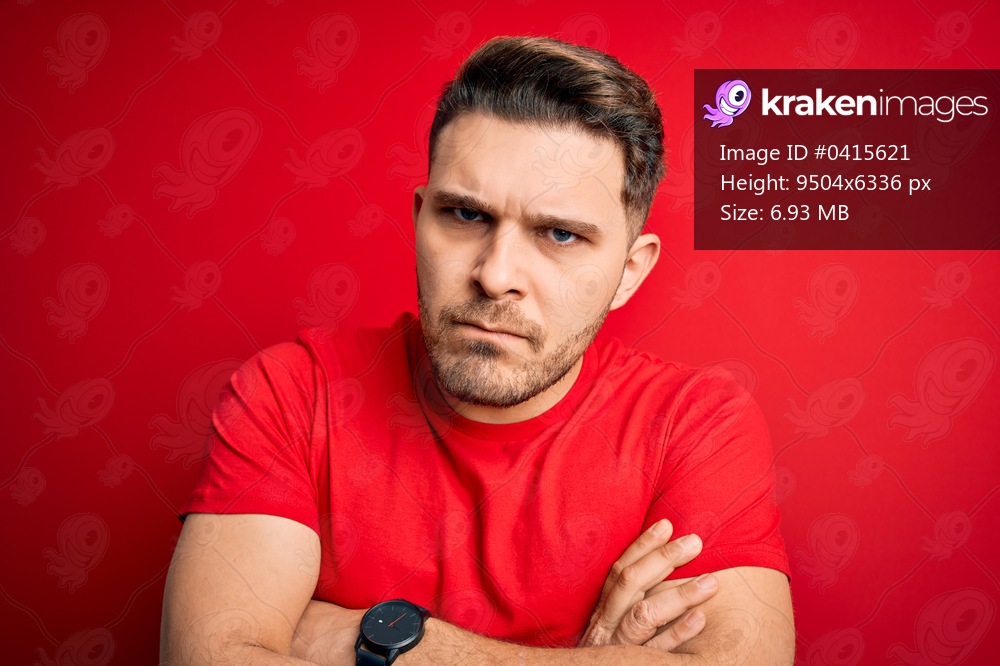 Young man with blue eyes wearing casual t-shirt over red isolated background skeptic and nervous, disapproving expression on face with crossed arms. Negative person.