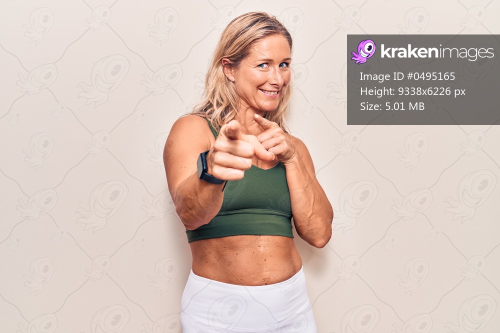 Middle age caucasian blonde woman wearing sportswear pointing fingers to camera with happy and funny face. good energy and vibes. 