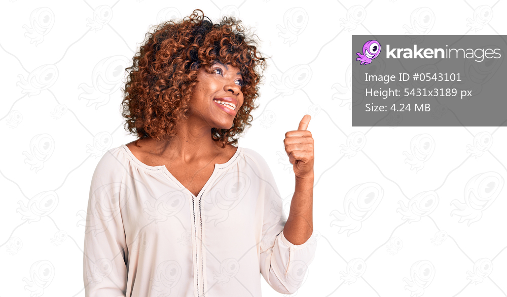 Young african american woman wearing casual clothes smiling with happy face looking and pointing to the side with thumb up. 