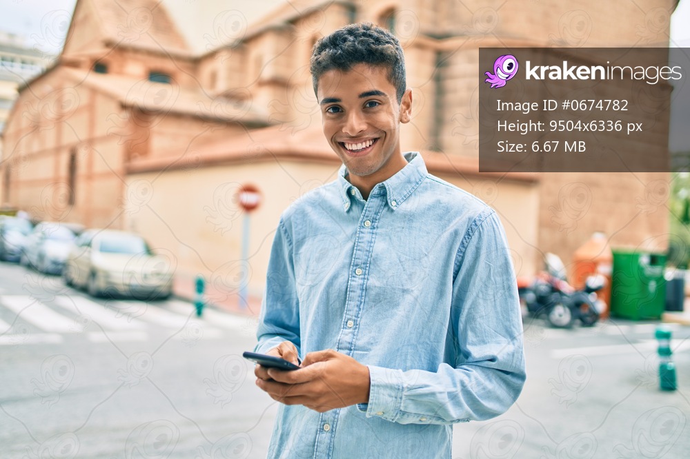 Young latin man smiling happy using smartphone walking at the city.