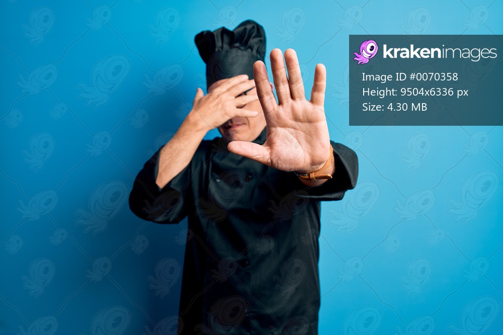 Middle age handsome grey-haired chef man wearing cooker uniform and hat covering eyes with hands and doing stop gesture with sad and fear expression. Embarrassed and negative concept.