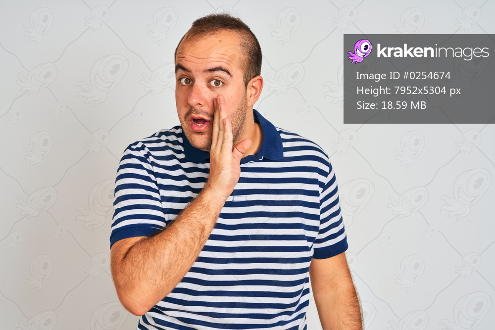 Young man wearing casual striped polo standing over isolated white background hand on mouth telling secret rumor, whispering malicious talk conversation